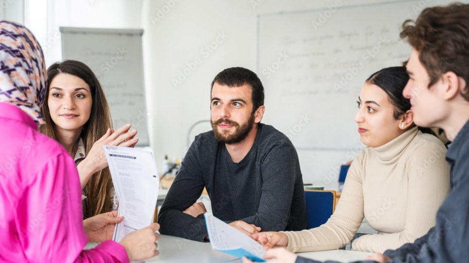 Gruppe von Menschen sitzt an einem Tisch und diskutiert, während sie Dokumente betrachten.